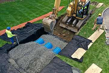 Excavator installs drainage pipes in a lined residential trench