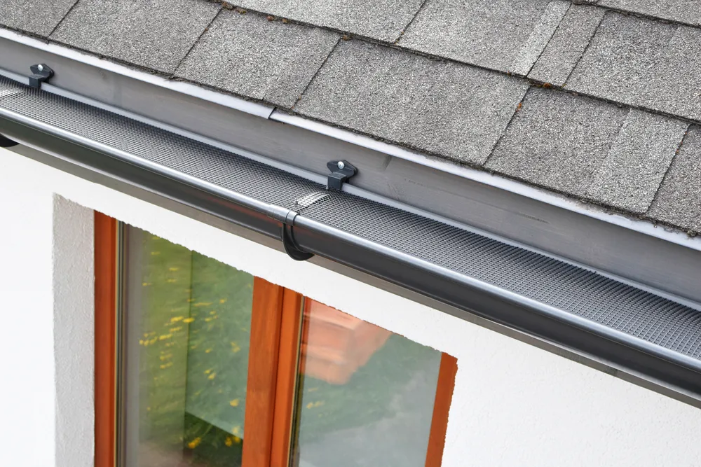 Plastic guard over new dark grey plastic rain gutter on asphalt shingles roof